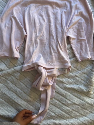 Ljusrosa topp med knyt framtill - Supersöt ljusrosa topp med trekvartsärm och knyt framtill. Tillverkad i mjuk bomull som känns skön mot huden. Perfekt för dig som gillar en feminin och avslappnad stil. Passar till både jeans och kjol.