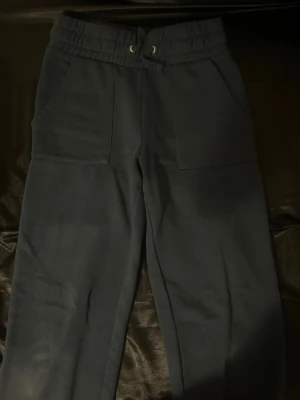 Mörkblå mjukisbyxor med dragsko - Säljer ett par mörkblå mjukisbyxor med bred resår i midjan och dragsko. Byxorna har två stora fickor framtill och är gjorda i mjukt, tjockt material som känns riktigt skönt. Perfekta för chill dagar eller när du vill vara extra bekväm.