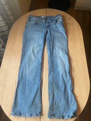 Ljusblå bootcut jeans  - Säljer ett par ljusblå bootcut jeans från H&M med klassisk femficksdesign och normalhög midja. Jeansen har en avslappnad passform och är tillverkade i mjuk denim med lite stretch. Perfekta för en chill och trendig look. Short length men det finns även ett litet hål.