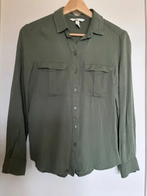 Olivgrön skjorta med fickor - En skjorta i viskos med krage, knäppning fram och bröstfickor med lock.  Knappt använd.  Från rökfritt hem men vi har hundar.