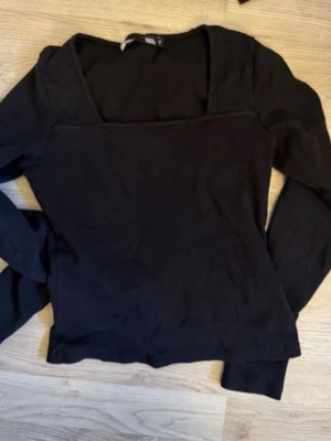 Svart långärmad topp 157 - Stilren svart långärmad topp från 157 med fyrkantig ringning. Tillverkad i mjukt ribbat material som sitter snyggt på kroppen. Perfekt att matcha med jeans eller kjol för en enkel men trendig look.