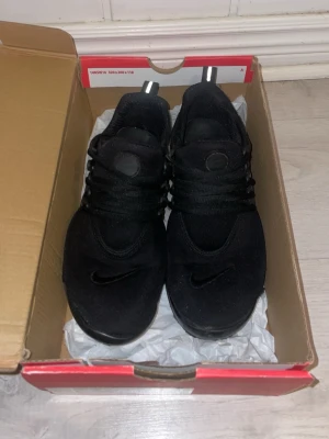 Svarta Nike sneakers i mesh - Säljer ett par helsvarta Nike sneakers med låg profil och klassisk Swoosh på tån. Skorna har ovandel i mesh för bra andningsförmåga och elastiska skosnören för skön passform. Perfekta för dig som gillar stilrena och sportiga skor.