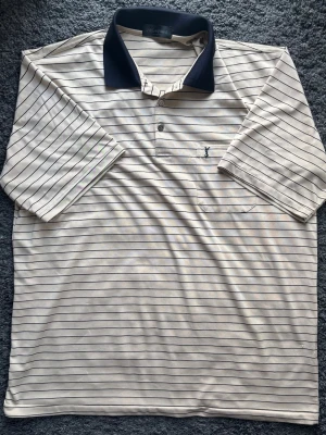 Lyxig Yves Saint Laurent 100% silke pikétröja - Klassiska Ränder & Sällsynt Vintage - Lyxig 100% siden YSL-piké, snygga horisontella ränder och mörkblå. Premium vintage!  👕Märke: Yves Saint Laurent  📏Storlek: L, regular fit.  🧵Material: 100% Premium Silke. Exklusivt och väldigt skönt. 📐Mått: Bröst 58cm, Längd 73cm. ✅Skick: 8/10 – Mycket fint och välbevarat vintage skick. Har några pyttesmå skavanker i sidenet (se bilder), syns ej vid användning. ✨Detaljer: YSL-logotyp knappar och broderad logo på fickan. Knappar. Mörkblå krage. Limited feel & sällsynt. ‼️Skickas inom 24h‼️ 