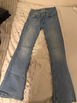 Ljusblå bootcut jeans - Säljer ett par ljusblå bootcut jeans med klassisk femficksdesign och dragkedja. Jeansen har en lätt tvättad look och utsvängda ben, perfekta för en avslappnad och trendig stil. Materialet är mjukt denim som ger en bekväm känsla hela dagen. Jeansen är från lager 157 och sparsamt använda. Storlek xs.