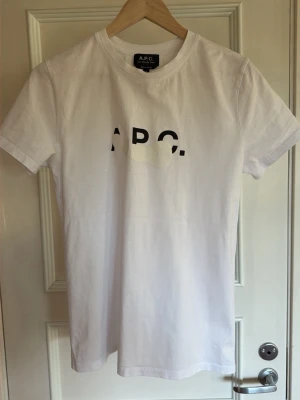 Vit t-shirt från A.P.C. med paint splatter. - Vit klassisk t-shirt från A.P.C. med svart tryck på bröstet med paint splatter för en modern look.     T-shirten har rund halsringning och korta ärmar. Tillverkad i mjuk bomull för en skön och avslappnad känsla. Perfekt till jeans eller shorts.