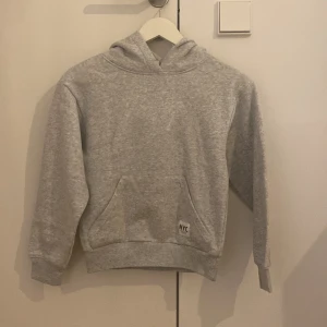 Grå hoodie från H&M  - En basic grå hoodie från H&M med klassisk känguruficka. På fickan sitter en liten vit lapp med texten 'NYC new york'.  Storlek 134-140🩶