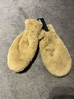 Beige fluffiga tumvantar Fideli Thumb - Supersköna och fluffiga beige tumvantar från Fideli Thumb. Vantarna har en mjuk pälsliknande yta som känns riktigt lyxig och värmande. Perfekta för kalla dagar när du vill hålla händerna varma och samtidigt se snygg ut.
