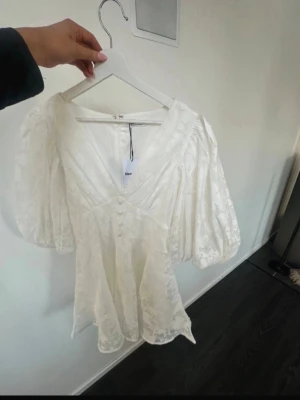 Vit kortklänning från Showpo - Supersöt vit kortklänning från Showpo med puffiga korta ärmar, v-ringning och dekorativa knappar framtill.  Perfekt för sommarens alla tillfällen! Samt studenten klänningen är k storlek M men skulle säga att den passar xs/s också. 