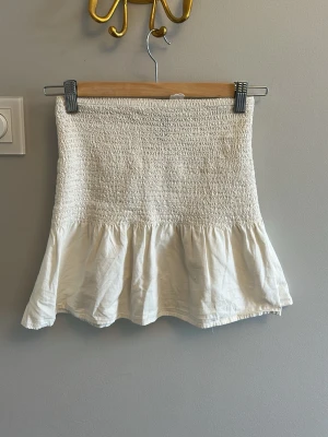 Vit volangkjol med smock - Supersöt vit kortkjol med smock upptill och volang nedtill. 