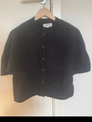 Svart poncho top från Gina  - Mysig svart poncho top från ginatricot i ullblandning. Koftan har rund halsringning, stora knappar framtill och en unik cape-liknande design över axlarna. Perfekt för lager på lager och en cool, avslappnad stil. Är slutsåld och ny pris är 500 kr💞