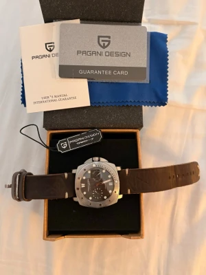 Pagani Design automatisk klocka brun - Snygg automatisk klocka från Pagani Design med rund urtavla i svart och silverfärgat rostfritt stål. Klockan har ett specialutgåva brunt läderarmband och synlig mekanism på baksidan. Levereras med originalkartong, manual och garantikort och originalarmbandet finns också med.
