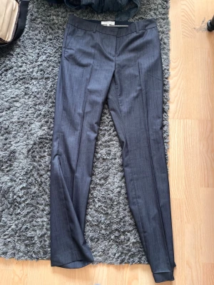 Mörkgrå kostymbyxor  - Snygga mörkgrå kostymbyxor med smal passform och pressveck. Byxorna har diskreta fickor och är tillverkade i ett tunt, elegant material som ger en stilren look.