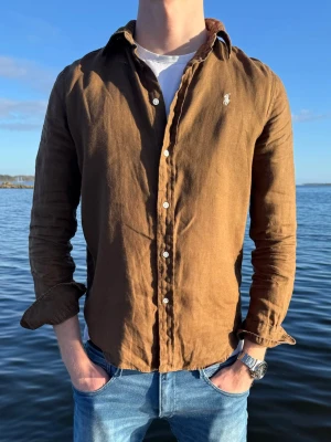 Brun linneskjorta från Ralph Lauren - Säljer en brun långärmad skjorta från Ralph Lauren i linne. Skjortan har klassisk krage, knappar framtill och den ikoniska broderade loggan på bröstet. Perfekt för dig som gillar en avslappnad men ändå stilren look. Storlek S men passar även M. Nyskick och vårt pris endast 449kr men kan gå ner vid snabb affär.🤩 // Studio II Resell 💙