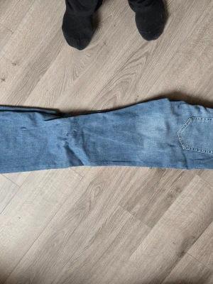 Blå bootcut jeans i klassisk modell - Säljer ett par mellanblå jeans med rak passform och klassisk femficksdesign. Jeansen har en enkel, tidlös look och är tillverkade i denim. Perfekta för dig som gillar en avslappnad stil. De har pyttelite slitage längst ner, se bild