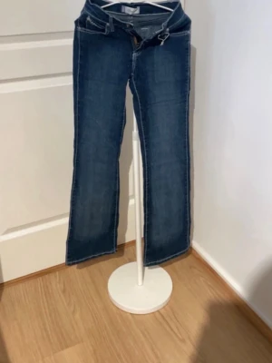Blå bootcut jeans med kontrastsömmar - Snygga blå bootcut jeans med ljusa kontrastsömmar och klassiska bakfickor med dekorativa detaljer. Jeansen har normal midja och är tillverkade i ett denimtyg med lätt stretch för skön passform. Perfekta för en avslappnad och trendig look.
