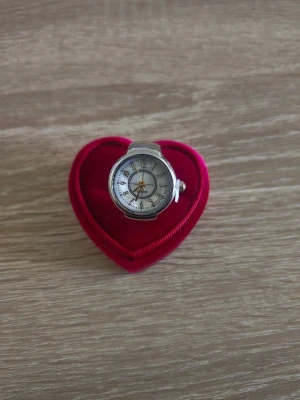 Unik silverfärgad ringklocka - Säljer en unik ringklocka i silverfärg med rund urtavla och tydliga siffror. Klockan har ett justerbart ringband och en klassisk analog visning. Perfekt accessoar för dig som vill sticka ut med något annorlunda och stilrent.