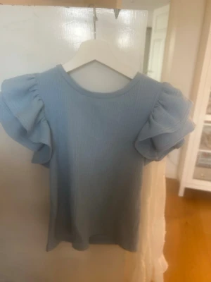 Ljusblå ribbad topp från Zara - Supersöt ljusblå topp från Zara med ribbad struktur och voluminösa, korta puffärmar. Perfekt för dig som vill ha en feminin och trendig look. Materialet känns mjukt och stretchigt, vilket gör den bekväm att bära hela dagen.