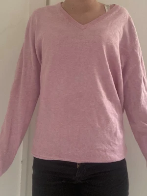 Ljusrosa V-ringad tröja Lindex - Ljusrosa långärmad tröja från Lindex The Essentials i mjuk bomull. Tröjan har en klassisk V-ringning och enkel, avslappnad passform. Perfekt att matcha med jeans eller kjol för en clean look.
