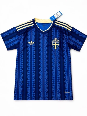 Blå Sverige fotbollströja Adidas - Snygg blå fotbollströja från Adidas med Sveriges landslagsemblem på bröstet och gula detaljer. Tröjan har ett unikt mönster i olika blå nyanser, gula ränder på axlarna och V-ringad krage. Tillverkad i lätt och ventilerande material, perfekt för träning eller match.