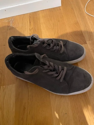 Vagabond i mocka - Snygga mörkgrå sneakers med ovandel i mocka och matchande grå skosnören. Skorna har en klassisk låg profil och vit sula som ger en clean look. Perfekta för dig som gillar stilrena och enkla sneakers till vardags.