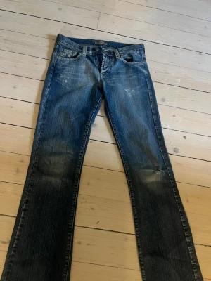 Blå bootcut jeans med slitningar - Ett par blå lågmidjade bootcut jeans från 2000s med snygga slitningar och tvättade detaljer. Klassisk femficksmodell med dragkedja och knapp. Jeansen har en utsvängd passform nertill.