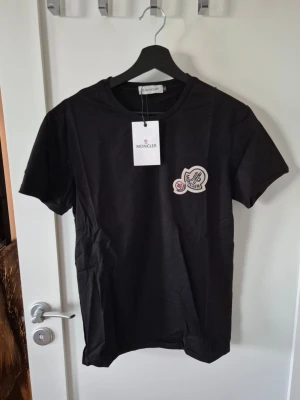 Svart Moncler t-shirt med logga - Snygg svart t-shirt från Moncler med klassisk rund hals och korta ärmar. På bröstet sitter en broderad Moncler-logga som ger en exklusiv känsla. Perfekt för dig som gillar stilrena och trendiga plagg.