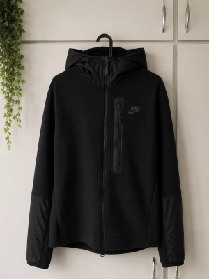 Svart Nike tech - Snygg svart tech från Nike med hel dragkedja framtill och huva. Tröjan har en bröstficka med dragkedja och diskret Nike-logga på bröstet. Materialet är lätt och vindtätt, perfekt för blåsiga dagar. Ärmarna har förstärkta partier för extra hållbarhet.