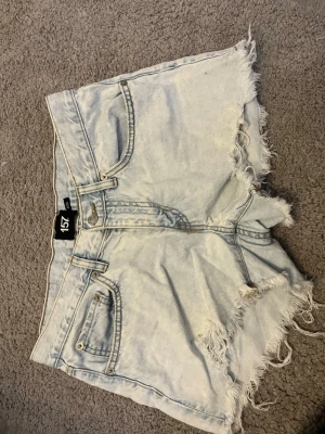 Ljusa denimshorts från 157 - Säljer ett par ljusblå denimshorts från 157 med fransiga kanter och klassisk femficksdesign. Shortsen har hög midja och råa avslut för en avslappnad look. Perfekta till sommaren och lätta att matcha med olika stilar.