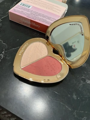 Charlotte Tilbury hjärtformat rouge - Rougepalett från Charlotte Tilbury i ett lyxigt hjärtformat guldigt etui med spegel. Innehåller två nyanser: en ljus beige highlighter och en varm rosaröd rouge. Perfekt för att skapa en fräsch och glowig look.