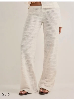 Vita virkade vida leggings - Säljer ett par vita virkade byxor med utsvängda ben och låg midja. De har en mjuk och stretchig känsla, perfekt för en avslappnad och trendig look. Materialet är virkat och ger en unik textur. Passar perfekt till sommarens outfits.