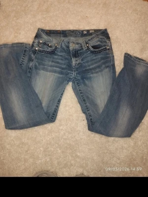 Blå bootcut jeans från True Religion - Säljer ett par blå bootcut jeans från miss memed slitningar och kontrastsömmar. Jeansen har klassiska fem fickor, låg midja och detaljerade sömmar på fickorna. Perfekta för en avslappnad och trendig look.