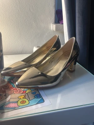 Guldiga klackar, pumps  - Snygga pumps i guld med spetsig tå och stabil blockklack. Storlek 39 men tyvärr för små för mig som vanligtvis har 39. Så mer som en 38/38,5 