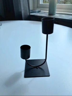 Svart metall ljusstake i modern design - Säljer en svart ljusstake i metall med två hållare i olika höjd. Ljusstaken har en fyrkantig bas och minimalistisk, modern form. Perfekt som inredningsdetalj för dig som gillar stilrena och enkla former.14cm hög