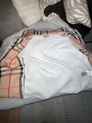 Burberry hoodie  - Snygg grå hoodie från Burberry med dragkedja och klassiskt beige, svart och rött rutigt foder på insidan. Mjuk och skön bomullsblandning, perfekt för en trendig och avslappnad look. Ikonisk Burberry-tag i nacken.