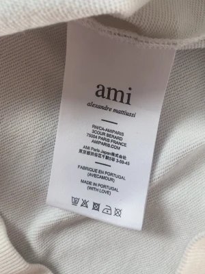  Ami Alexandre Mattiussi - Säljer en stilren vit hoodie från Ami Alexandre Mattiussi. Hoodien har en broderad detalj framtill och är tillverkad i mjukt material. Klassisk passform med ribbade muddar och en skön huva. Perfekt för dig som gillar minimalistisk design.