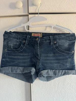 Korta låg midja blå denimshorts med upprullad kant - Säljer ett par klassiska blå jeansshorts från in denim uniq young we trust. Shortsen har upprullad kant och är låg midja och korta. Snygg tvättad denimlook och normal passform. Perfekta till sommaren!