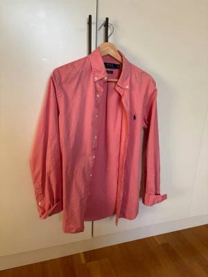 Ralph Lauren skjorta - Klassisk rosa skjorta från Polo Ralph Lauren med button-down krage och broderad logga på bröstet. Skjortan har långa ärmar och knäppning framtill. Nästintill ny använd fåtal gånger. Tags och qr kod finns. Storlek S/M