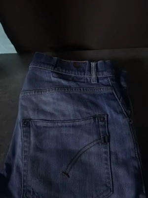 Blå jeans från Dondup - Säljer ett par klassiska blå jeans från Dondup med snygga slitningar och detaljer på fickorna. Jeansen har normal passform och är gjorda i bomull. Perfekta för dig som gillar en avslappnad och cool stil.