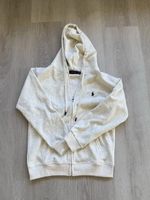 Polo Ralph Lauren grå ziphoodie - En skön grå Polo Ralph Lauren ziphoodie som är perfekt till sommaren som inte är nån tjock hoodie utan tunn som man kan matcha med en vit tröja under, officellt från Ralph Lauren EU hemsida, pris kan alltid diskuteras 