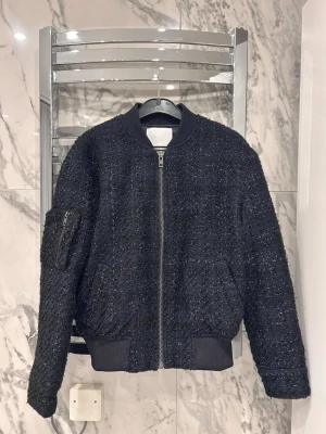 Samsøe samsøe jacka    - Säljer en jacka från samsøe samsøe i storlek XS. Jackan är svart/mörkblå glittrig. På ena ärmen har den en ficka med dragkedja. Den har även fickor och knappar vid armarna. 