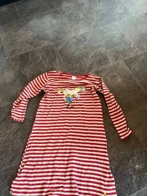 Rödvit randigt nattlinne med Pippi - Nattlinne med röda och vita ränder, lång ärm och rund hals. Tryck framtill med Pippi Långstrump och Lilla Gubben. Mjuk och bekväm bomullskvalitet, perfekt för mysiga kvällar. Klassisk och lekfull design som sticker ut. (Plus frakt) 