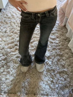 Gråa bootcut jeans med vita sömmar - Säljer ett par mörkgråa bootcut jeans med vita kontrastsömmar och låg midja. Jeansen har klassisk femficksdesign och på fickorna är det små rosa paljetter. Dem är ifrån Gina tricot 14+ i storlek xs💓dem är aldrig använda men prislappen är borttagen 