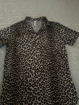Leopardmönstrad skjorta med krage - Snygg skjorta med leopardmönster i svart och beige. Skjortan har korta ärmar och klassisk krage, perfekt för dig som vill sticka ut. Lätt och luftig känsla, passar till många olika stilar.