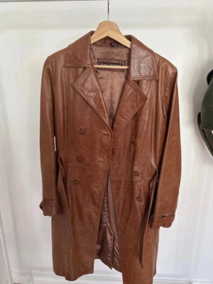 Brun skinn trenchcoat vintage - Snygg brun lång kappa i äkta skinn från Bruno Zaragoza i fint vintage skick! Storlek 38. :)