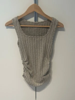 Ribbad grå linnetopp S - Snygg ribbad linnetopp i grått med rynkdetalj på sidan. Toppen är ärmlös och har en rundad halsringning. Perfekt att styla till jeans eller kjol för en chill look.
