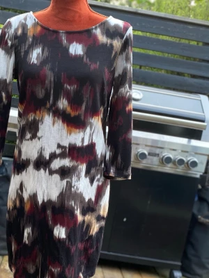 Mönstrad långärmad klänning - Klänning från Vila med långa ärmar och dragkedja baktill. Klänningen har ett abstrakt mönster i olika färger. Längd: 90 cm Bystmått: 48 cm  Inga bilder på mig! Katter finns i hemmet!