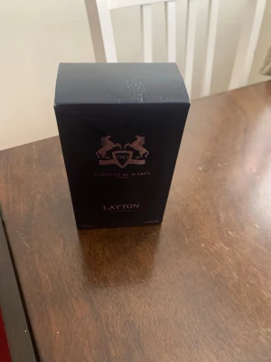 Layton parfym från Parfums de Marly - Exklusiv parfym i mörkblå kartong från Parfums de Marly, modellen Layton. Förpackningen har eleganta detaljer i silver och rosa samt ett stilrent lejonemblem. Innehåller 125 ml Eau de Parfum med lyxig och modern känsla.