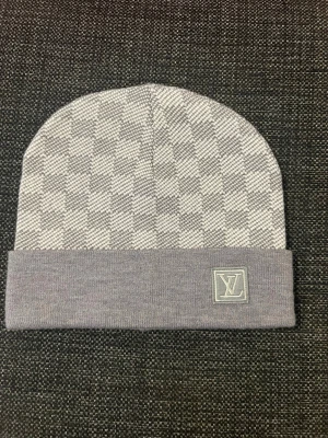 Grå Lmössa med  - Snygg grå mössa  med klassiskt rutmönster och vikt kant. logga framtill på en patch. Tillverkad i mjukt stickat material som känns lyxigt och bekvämt. Perfekt accessoar för att lyfta din stil under kyliga dagar.