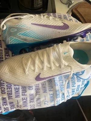 Nike Air Zoom Mercurial fotbollsskor - Säljer ett par Nike Air Zoom Mercurial fotbollsskor i vitt med lila Swoosh och blå detaljer. Skorna är använda totalt 3 gånger på endast fotbollsträning, vid någon typ av funderingar så är det bara att skriva priset kan absolut diskuteras!👊🏼