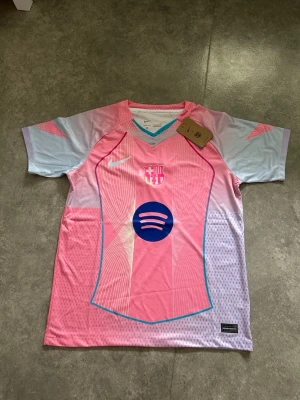 Barça rosa matchtröja Nike - Snygg FC Barcelona matchtröja i rosa och ljusblått från Nike. Tröjan har korta ärmar, V-ringning och klubbmärke samt sponsorlogga på bröstet. Tillverkad i lätt och ventilerande funktionsmaterial, perfekt för fotboll eller träning.